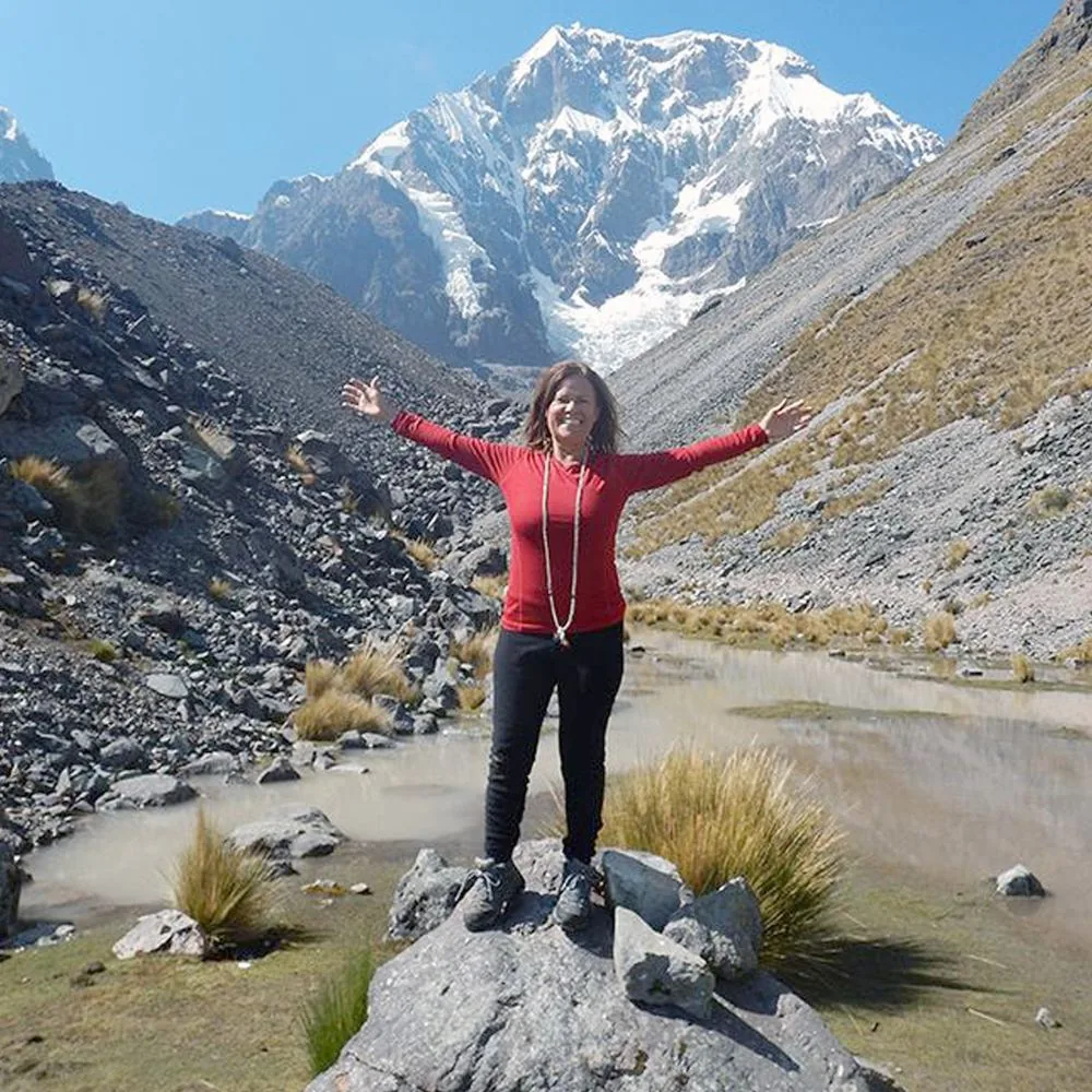 Isa Herrera standing high in the Andes mountains in Peru, arms thrown wide, small against the mountainside.